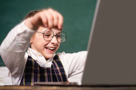 Back to school and home schooling. Excidet pupil working on laptop computer over blackboard background. Educational process. Kid school. Happy cute clever boy pupil with book.の写真素材