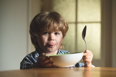 Baby eating food on kitchen. Cute kid are eating. Laughing cute child baby boy sitting in highchair and eating on blurred background.の写真素材