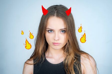 Angry cute devil. Fashion portrait of a beautiful young woman posing over white background. Close up...