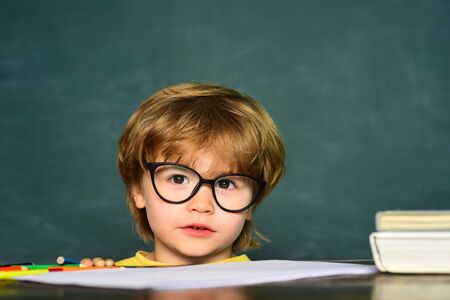 Cute little preschool kid boy in a classroom. Blackboard background. Teachers day. Kids from primary school. September 1 - Classroom.の写真素材