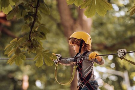 Happy child climbing in the trees. Children summer activities. Early childhood development. Child. Safe Climbing extreme sport with helmet.の写真素材