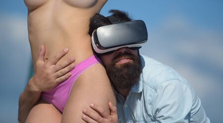 The world of erotic virtual reality. Bearded man in virtual reality headset hugging sexi topless woman. Hipster wearing virtual reality device touching sexy girl body. Adult virtual reality gamesの写真素材