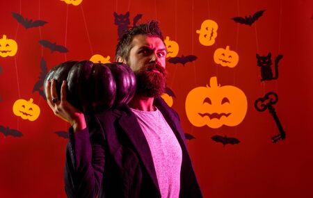 Halloween man with pumpkin in darkness. Evil witcher with red hair and a beard in a black cloak reading a book of spells. Halloween, holidays celebration.の写真素材