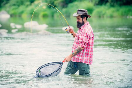 Holding brown trout. Man with fishing rods on river berth. Men fishing in river during summer day....