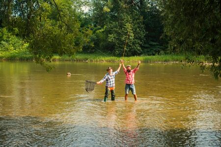 Generations ages: grandfather and father. Fisherman fishing in a river with a fishing rod. Still...