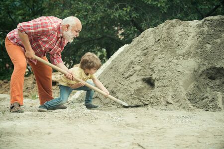 Child and works. Little son worker with shovel. Little son helping his father with building work. Childhood concept. Future worker son with father.の写真素材