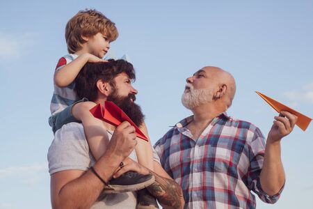Happy grandfather father and grandson with toy paper airplane over blue sky and clouds background. Father and son playing outdoors. Fathers dayの写真素材