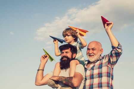 Happy child playing outdoors. Happy man family have fun together. Kids playing with simple paper planes on sunny day. Father giving son ride on back on blue sky background.の写真素材