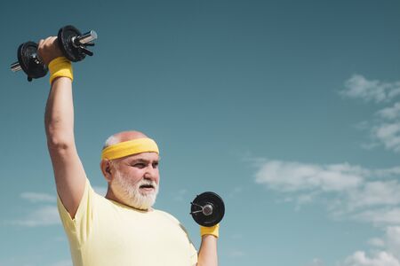 Elderly man practicing sports on blue sky background. Healthy lifestyle concept. Senior sportsman in...