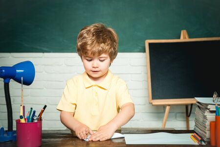 Elementary school and education - school concept. Kid with a book. Funny little child having fun on blackboard background. School concept. Happy cute clever boy pupil with book.の写真素材