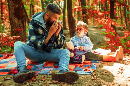 Cold flu season, runny nose. Cute boy with Father on Fall Nature Background. Childhood concept. Father with handkerchief.の写真素材