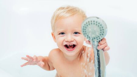 Childs hygiene. Happy baby playing with water and foam in a big kitchen sink. Health care and...
