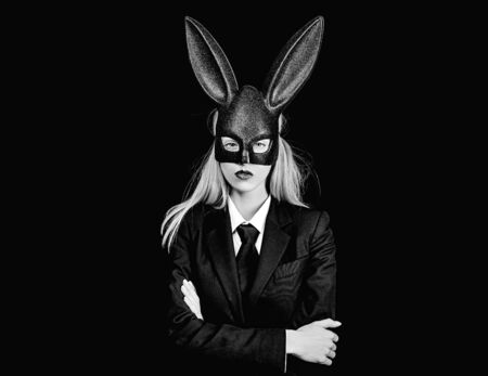 Easter woman. Sexy woman with mask Easter bunny on a black background and looks very sensually. Happy woman in bunny ears with easter egg.の写真素材