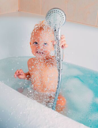 Cute baby in soft bathrobe after bath playing in kids room. Pleasant little kid playing in bath tube. Baby bathing toys.の写真素材
