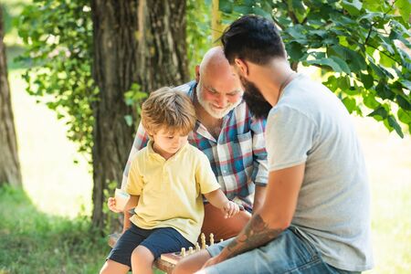 Cute boy developing chess strategy. Father son and grandfather relaxing together. Golden age...