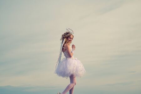 Teenager Cherub Cupid. Festive Art Greeting Card. Innocent Girl with angel wings standing with bow and arrow against blue sky and white clouds. Love card.の写真素材