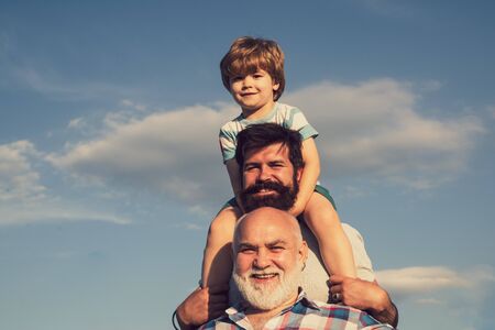 Happy fathers day. Grandfather playtime. Young boy with father and grandfather enjoying together in park on blue sky background.の写真素材
