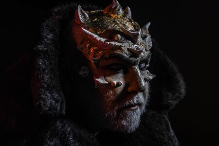 Severe king of perpetual cold kingdom wearing black fur coat. Magical creature with horns on head and golden dragon skin, supernatural concept. Demon head with thorns on face over dark backgroundの写真素材