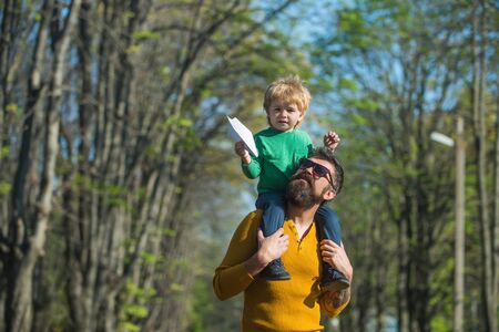 Father give son piggyback launching paper plane toy. Little child play with toy in park. Up, up, and awayの写真素材