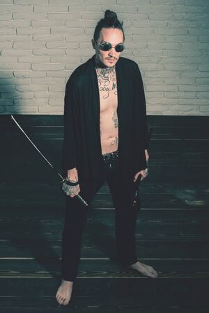 Warrior in black sunglasses and open clothes showing tattooed torso