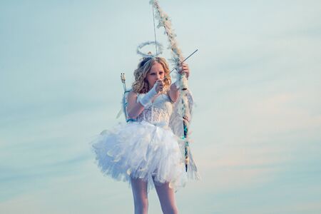Girl angel with halo in white angel dress. Enjoying magic moment. Portrait of little curly blond...