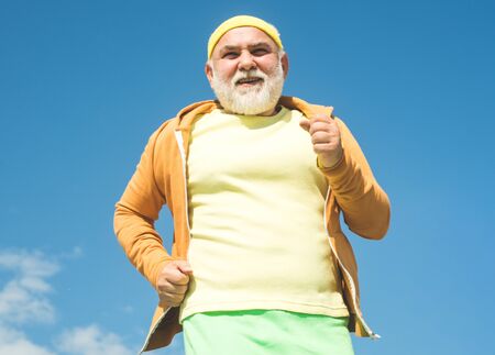 Elderly man practicing sports on blue sky background. Elderly man jogging. Golden age grandfather....