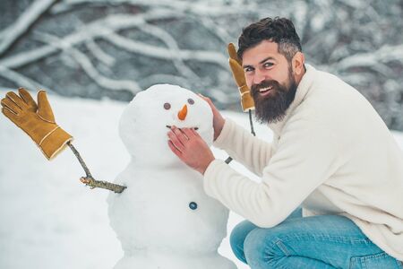 Funny snowmen. Happy smiling man make snowman on sunny winter day. People in snow. Snowman. Handsome Winter Man with snowman in frosty winter Park.の写真素材