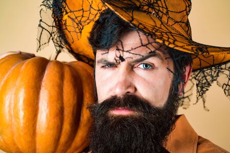 Halloween beaded man hold pumpkin - portrait. Halloween Man posing with pumpkins. Bearded Halloween man in witch hat - studio shot close up.の写真素材