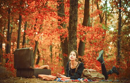 Beautiful girl lies on autumn background. Happy young woman are preparing for autumn sunny day. Attractive blonde woman in park, on blurred golden green trees background. Autumn time.の写真素材