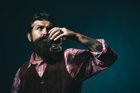 Alcoholic beverage. Confident bearded man in black suit with glass of whisky in loft. Man drinking alcohol from glass. Stylish rich man holding a glass of old whisky.の写真素材