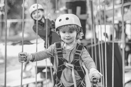 Happy little boyn calling while climbing high tree and ropes. Eco Resort Activities. Go Ape Adventure. Roping park. Toddler age. Hiking in the rope park boy in safety equipment.の写真素材