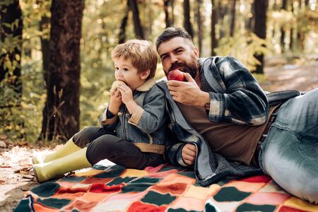 Healthy lifestyle. Nature picnic. Healthy snack. Vitamin charge. Family picnic. Hipster bearded dad with son spend time in forest. Brutal bearded man and little boy eat apples. Forest picnic hikingの写真素材