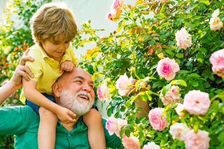 Happy grandfather giving grandson piggyback ride on his shoulders and looking up. Grandfather...