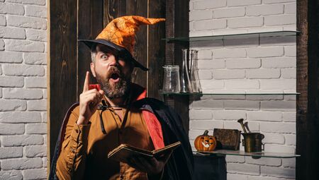 Scary face man with horror Make up holding Pumpkin head jack lantern on sky background. Evil witcher with red hair and beard in a black cloak reading a book of spells. Halloween, holidays celebration.の写真素材