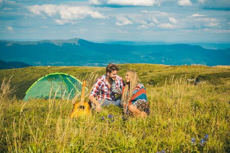 Enjoying the beautiful landscape of couples camping in the mountains. Happy couple tourists man and woman having a rest beside camp, guitar and sunny day.の写真素材