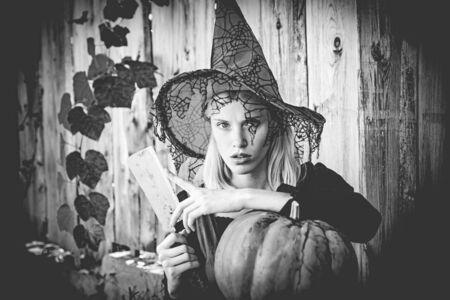 Witch Girl preparing to cut a pumpkin on wood background. Concept of Halloween. Close-up portrait of...