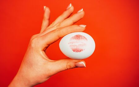 Print of red lips on white egg. Red lip imprint on easter egg on red background. Lipstick kiss...