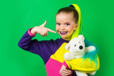 Little model with colored hair embracing and pointing on Teddy Bear. The concept of childrens...