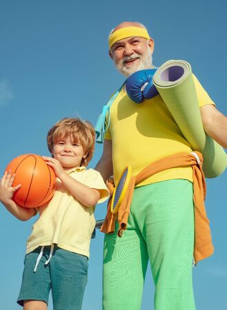 Sports coach and kid with basketball ball. Like sports. Different generations. Outdoor activities and healthy lifestyle. Grandfather giving grandson ride on back in park.の写真素材