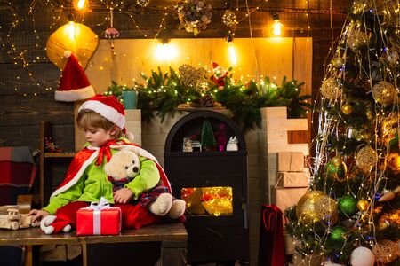 Christmas tree and new year decorations. Little boy sitting on a wooden table and playing with...