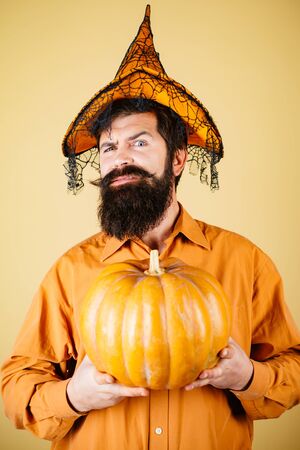Smiling happy man with pumpkin. Devil man. Thanksgiving day cooking. Young man with witch hat ready to Halloween party. Halloween Man posing with pumpkins.の写真素材