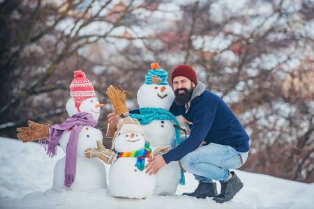 Happy hipster winter portrait. Handsome bearded man, father in winter clothes. Winter emotion. Funny snowmen. Happy father playing with a snowman on a snowy winter walk.の写真素材