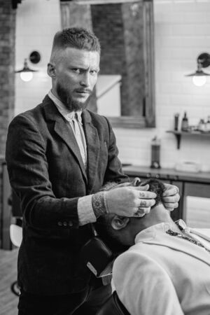 Professional hairstylist in barbershop interior. Senior man visiting hairstylist in barbershop. Barber - Shaves and Trims. Hair style and hair stylist.の写真素材