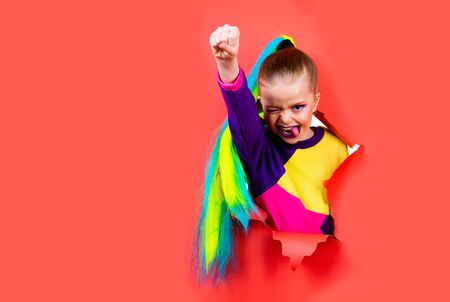 Schoolgirl superhero concept. Brave girl is breaking through color paper wall. Kid hand squeezed into a fist. Trendy clothes and hairstyle ponytail. Girl ready to school. Digital native generation.の写真素材