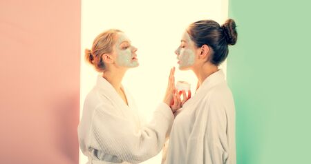 Young beautiful blonde women applies clay mud mask at face of her friend. Organic natural cosmetic for smooth pure skin. Natural beauty and healthy look concept.の写真素材