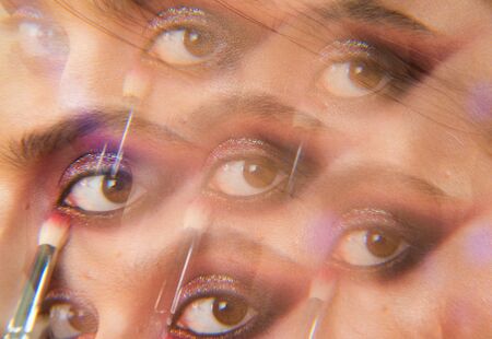 Kaleidoscopic photo of womans beautiful eye with purple smokey makeup. Glossy and shiny glitter for...