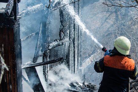 Real brave hero combat the fire with foam extinguisher. Strong and brave firefighter saving burning...