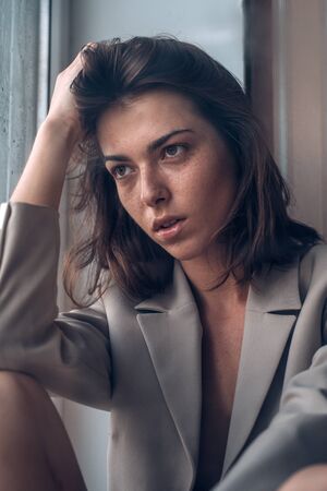 Sadness and disappointment. Depressed young woman sitting by the window. Close up.
