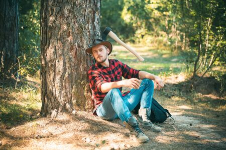 The Lumberjack working in a forest. Handsome Woodworkers lumberjack plaid shirt holding the axe on green nature background. A handsome young man with a beard carries a tree.の写真素材