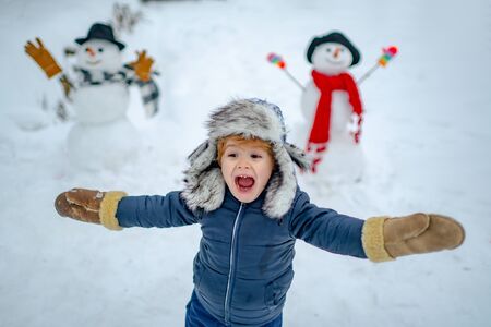 Happy kid winter portrait. Kids in snow. Happy child playing with a snowman on a snowy winter walk. Child playing with snow in park on white snow background.の写真素材